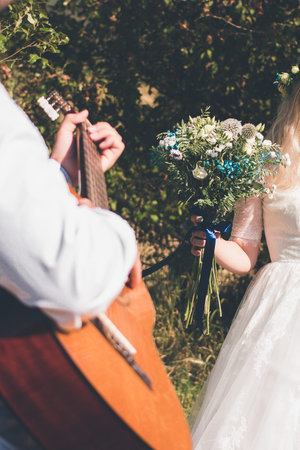 Groom plays the guitar, bride holds a wedding bouquet. Vertical orientation, no facesの写真素材