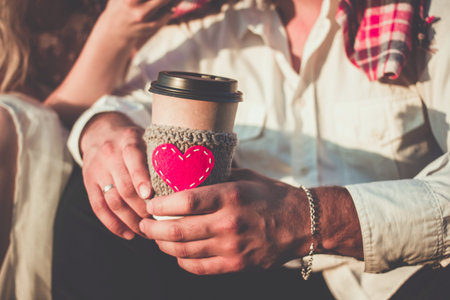 Romantic couple hugging while having picnic in sunset light. Coffee cup cozy knitted sleeve with felt red heart.の写真素材