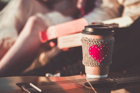Romantic couple hugging while having picnic in sunset light. Coffee cup cozy knitted sleeve with felt red heart.の写真素材