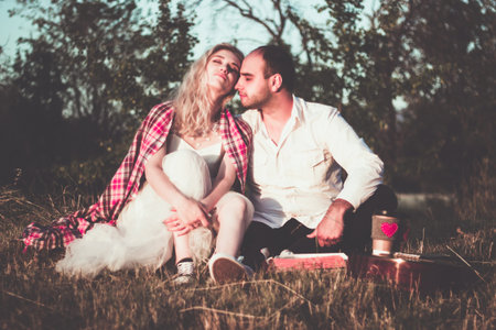 Romantic couple hugging while having picnic in sunset light. Handsome bearded man with guitar and...