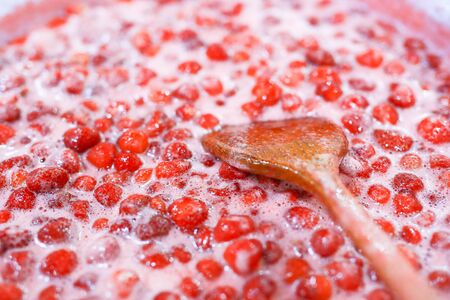 Strawberry jam cooking process. Wooden spoon liying on jam surface. Organic traditional jam manufacturing.の写真素材