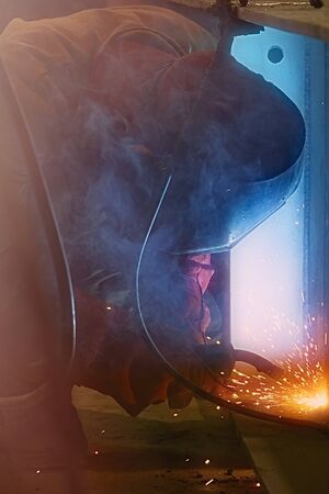 Welder uses welding machine to make sparks during manufacture of metal construction.の写真素材