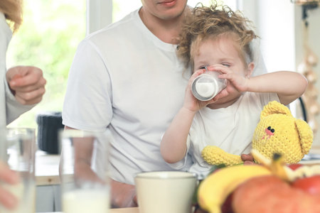 Cute little girl with her father drinking milk over window background. Vitamine breakfast in bright kitchen room interior. Happy family concept.の写真素材