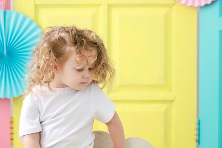 Pretty little blonde curly girl portrait in white t-shirt on yellow background.の写真素材