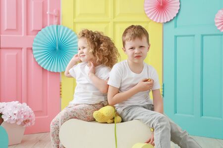Pretty little blonde curly girl and upset boy portrait in white t-shirt on yellow, pink and blue background. Kid gender relations concept.の写真素材