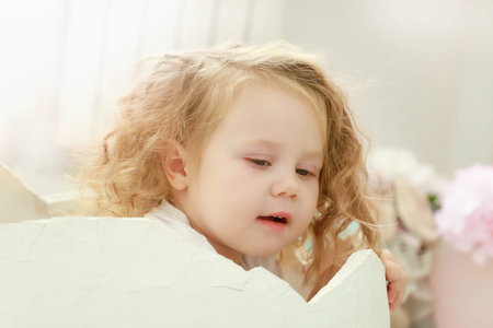 A little toddler kid is sitting in a white egg that hatched against a studio colorful background for a newborn portrait or family concept.の写真素材