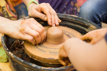 A close up view on ceramic production process on potters wheel with children. Clay crafts with kids concept.の写真素材
