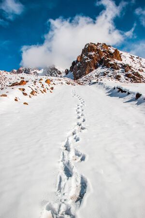 Deep marks in white snow. Snow tops and clouds amid blue skies. Winter mountain travel conceptの写真素材