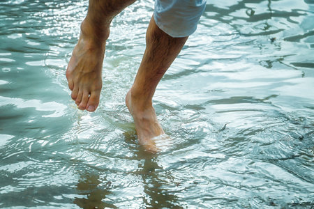 Barefoot man legs in cold mountain lake waterの写真素材