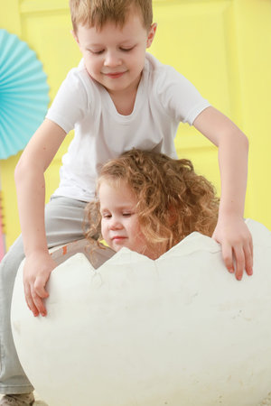 Older brother take care about his little sister is sitting in a white egg that hatched against a...