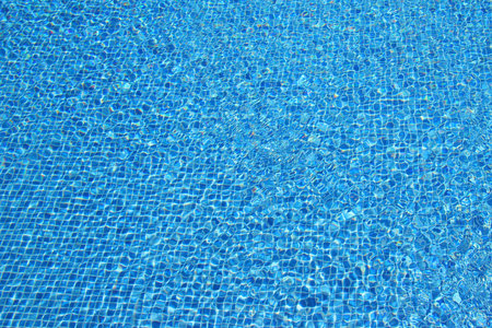 Top view of clear water in a blue tile pool background. Ripple effect