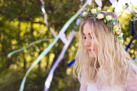 Beautiful blonde young bride portrait with wreath on her head in white wedding dress outdoor in summer, soft focusの写真素材