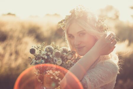 Beautiful young woman portrait in a white dress in boho style with a floral wreath in the summer in the field. Selective soft focus.の写真素材