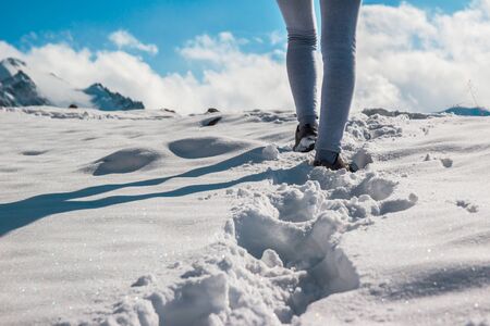 The legs of a young woman in sporting winter shoes in deep snow. Blue sky.の写真素材