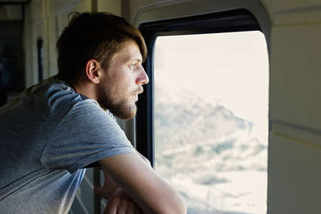 Middle plane portrait of a handsome young caucasian man with a beard, looks outside of the train's window, looking bored or tired of traveling too long.の写真素材
