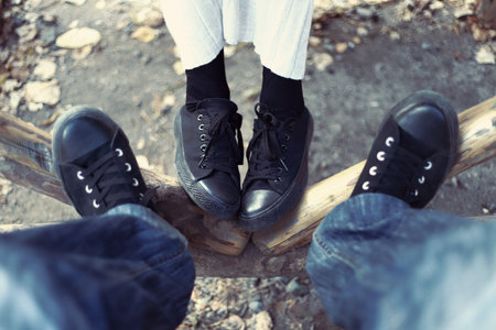 A close-up photo of a woman and a man in black sneakers on a background of logs. Date concept