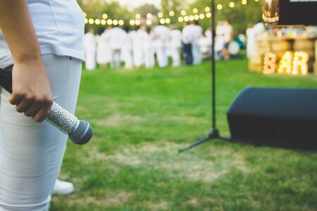 A slender woman in white clothes with a microphone in her hand stands on the background of people.の写真素材