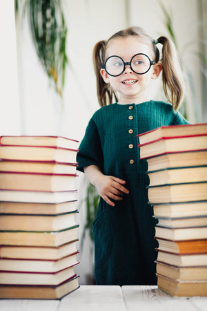 Cute smart preschool girl reading books in library or at home. Kids early learning and home...