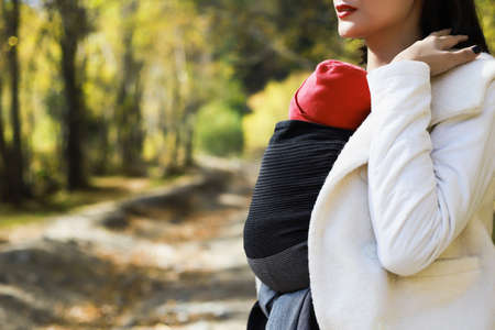 Beautiful young mother with her infant baby in sling outdoor. Babywearing conceptの写真素材