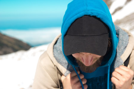 A bearded man in a black cap in the mountains. Hands compressed into a fist.
