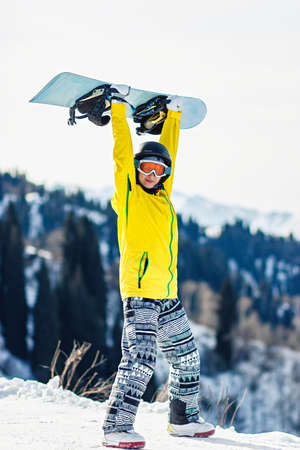 Young woman holds a snowboard over her head on a background of mountains.の写真素材