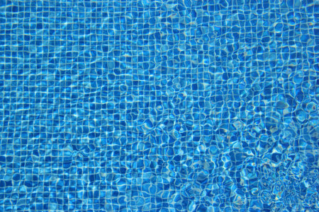 Top view of clear water in a blue tile pool background. Ripple effect.