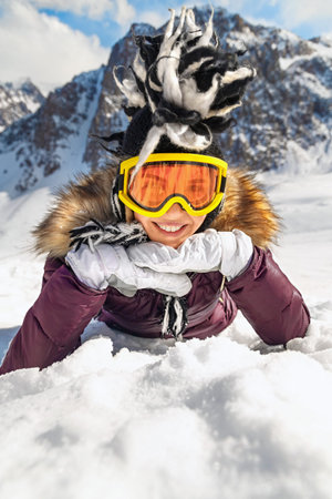Portrait of playful hipster woman lying on snowy at mountain or hill top in sunny day with blue sky...