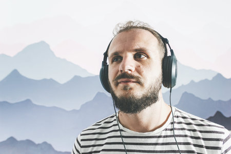 Meditative bearded happy man in a striped T-shirt listens to music with big headphones. looks to the...