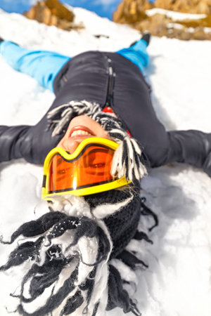 Portrait of pretty hipster woman lying on snowy at mountain or hill top in sunny day with blue sky...