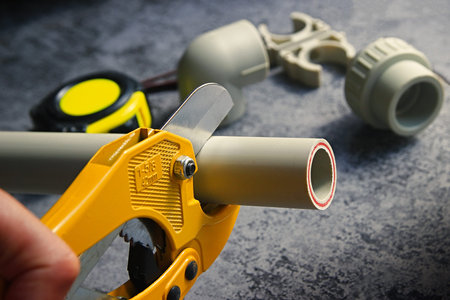 Close-up of plumbers hand with yellow scissors cutting pvc pipe. Heating systems and water supply...
