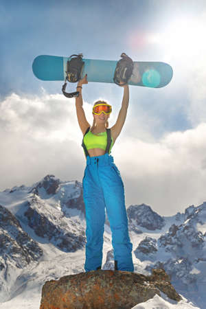 Laughing young woman in a swimsuit holding a snowboard in her hands in winter. Extreme sport. Cheerful snowboarder. Woman and sport.の写真素材
