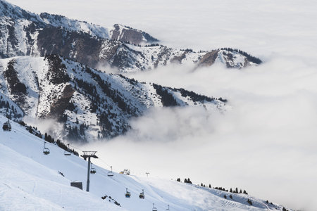 Ski resort in Cloudy Tian Shan mountains in the mist. Ski lift on the slope. Almaty holiday concept...