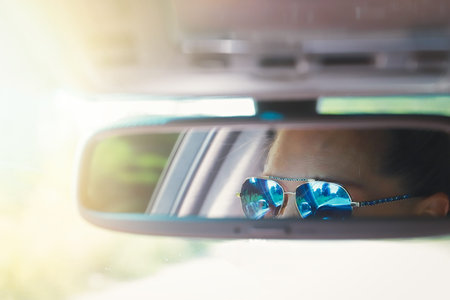 Woman in sunglasses is reflected in the cars rearview mirror
