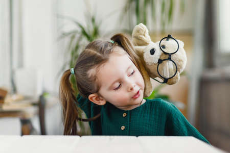 Sweet little girl is playing with a muppet bear in round shaped glasses and smiling while stay at homeの写真素材