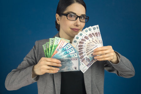 Young beautiful woman in glasses looks at camera with Kazakhstan tenge and Russian rubles in her hand. Selective focusの写真素材