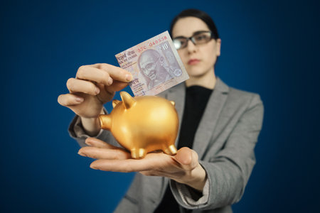 Woman in gray jacket with an Indian rupee and a piggy bank in her handsの写真素材