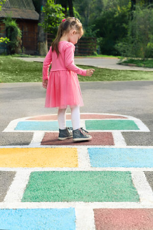 Little girl in a pink dress playing hopscotch on playground outdoors, children outdoor activities.の写真素材