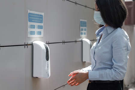 Young woman wearing a protective medical face mask and sanitizer on the outdoor wall in public placeのeditorial素材