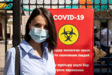 Young woman outdoor portrait wearing a protective medical mask on covid-19 social red banner backgroundのeditorial素材