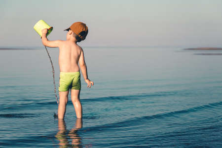 Boy playing in the sea with water and a bucketの写真素材