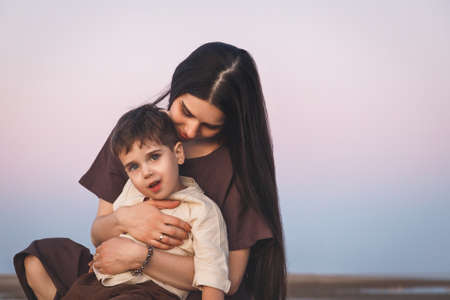 Gentle portrait of a young mother with her little son. Golden hour shot at sunset outdoorsの写真素材