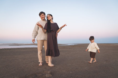 Young family with a three year old son walks barefoot along the wild evening beach. Family look linen clothesの写真素材