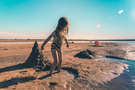 Little cute girl in a knitted swimsuit playing with sand on the seashoreの写真素材