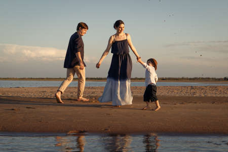 Little boy in brown panama walking on the beach with his parentsの写真素材