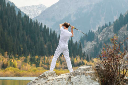 A young man stands on a large stone and holds a Japanese sword in his handsの写真素材