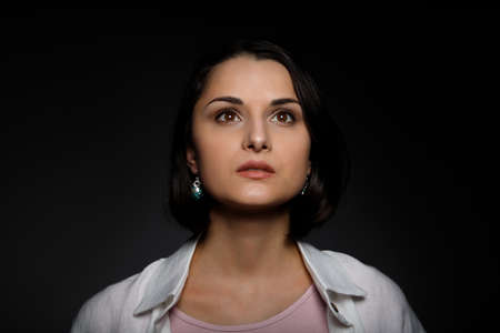 Low key portrait of serious young brunette multiethnic woman in pink tank and white shirt looking up.の写真素材