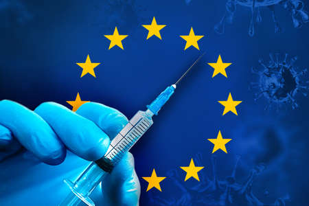 Hand in a blue rubber glove holds a syringe with virus vaccine in front of EU flagの写真素材