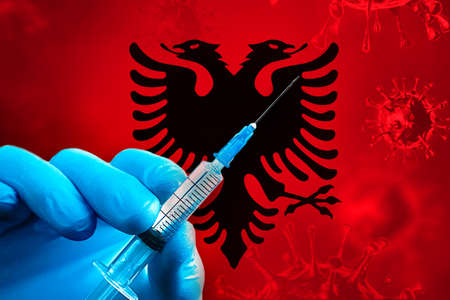 Hand in a blue rubber glove holds a syringe with virus vaccine in front of Albania flagの写真素材