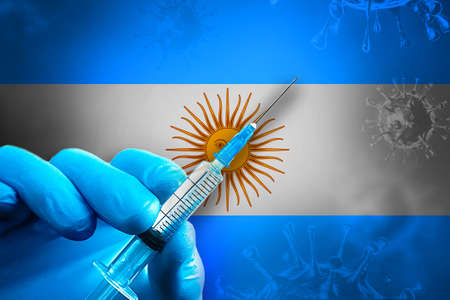 Hand in a blue rubber glove holds a syringe with virus vaccine in front of Argentina flagの写真素材