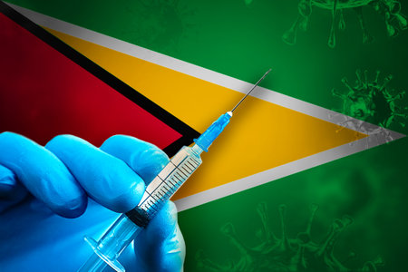 Guyana Covid-19 Vaccination Campaign. A hand in a blue rubber glove holds a syringe with covid-19 virus vaccine in front of Guyana flag. Coronavirus vaccination conceptの写真素材